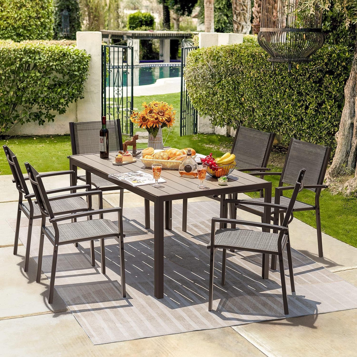 Outdoor dining set with table and chairs on a patio, featuring a pool and garden in the background.