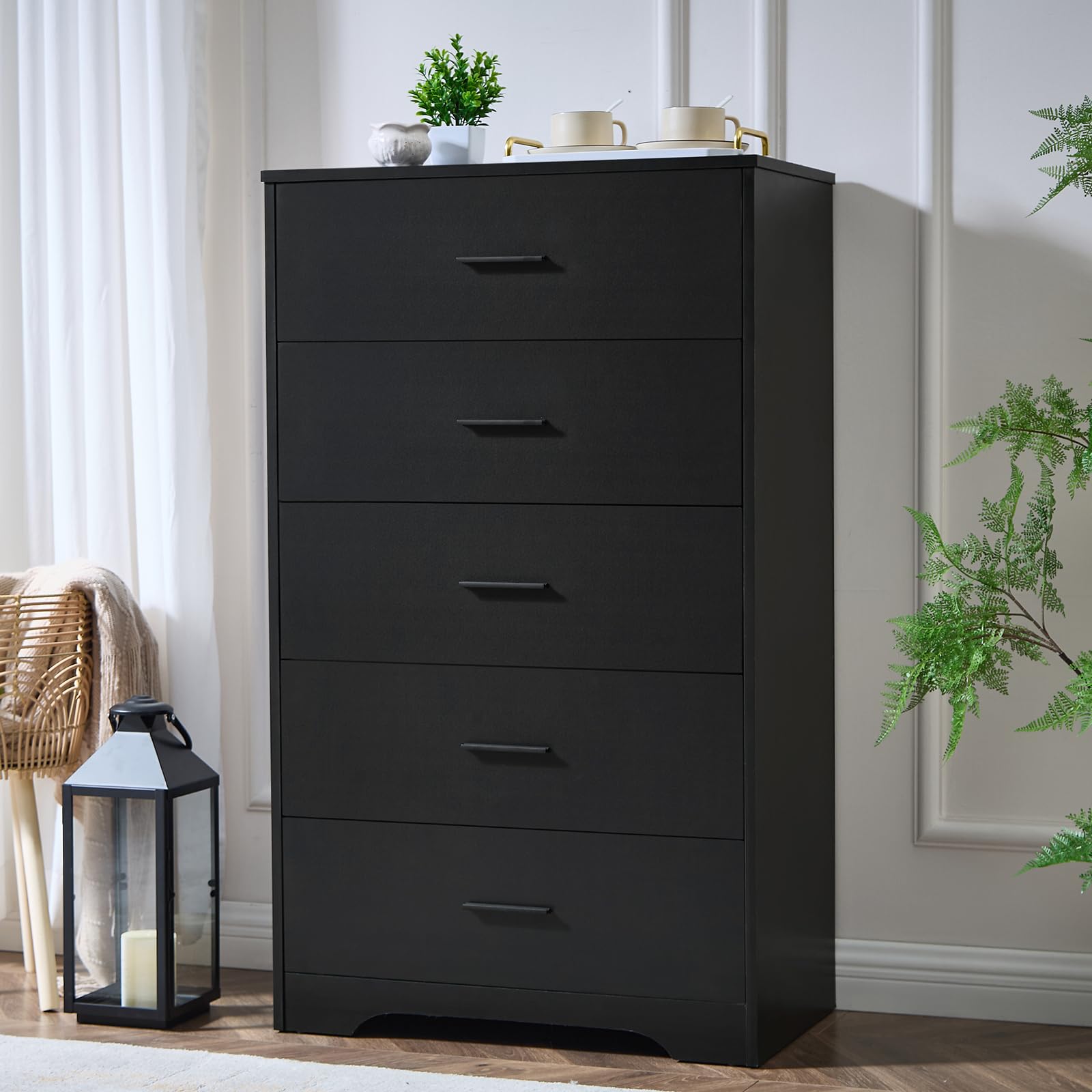 Black dresser with five drawers in a room setting with plants and a candle lantern.