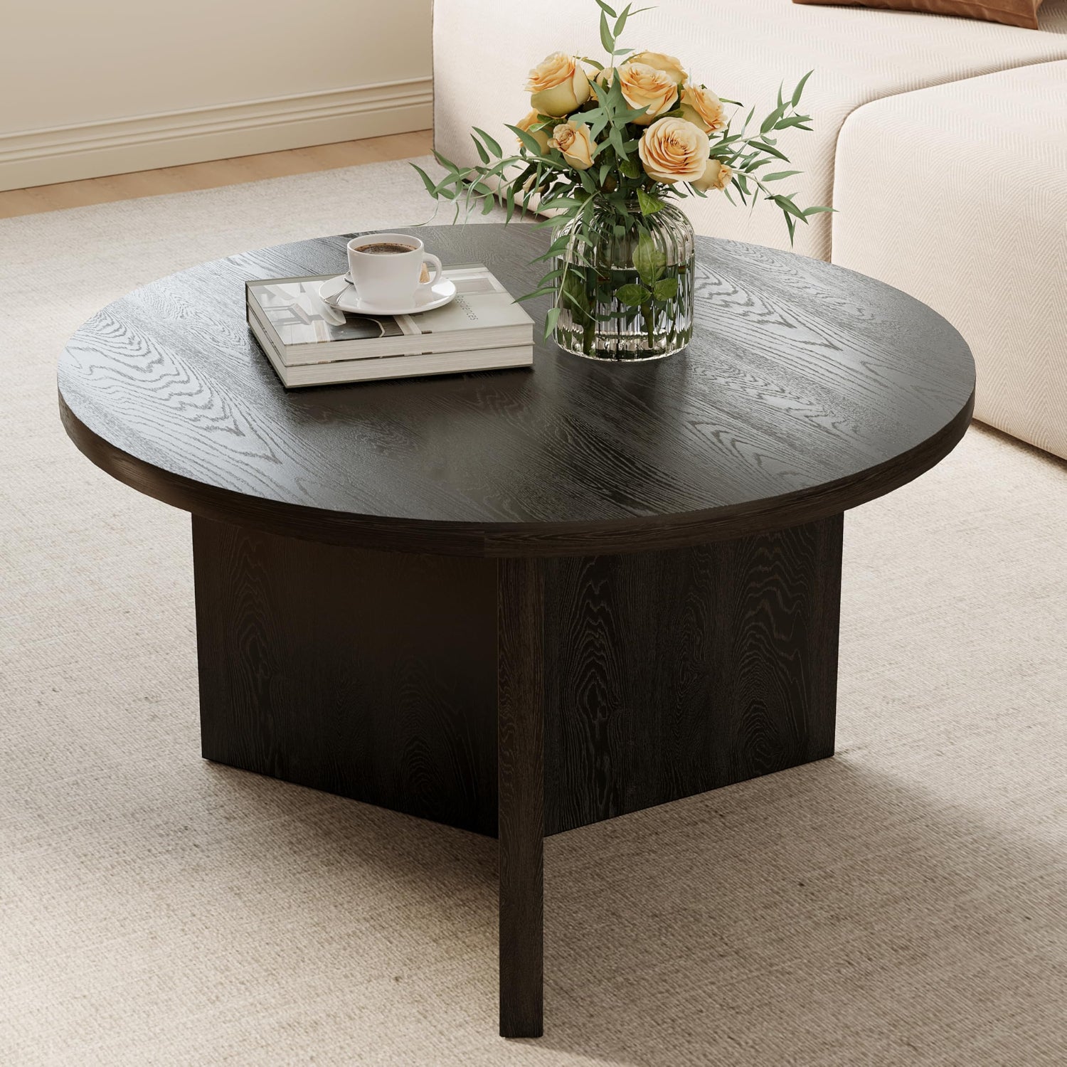 Round dark wood coffee table with a cup, books, and flowers on top in a living room setting.